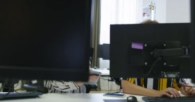Başlangıç ofisinde iki genç iş arkadaşı bilgisayar kullanıyor ve birlikte konuşuyorlar.
