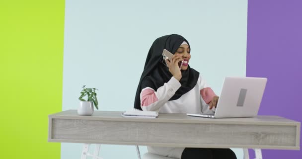 Bella e felice donna in sciarpa testa hijab utilizzando il telefono cellulare con computer portatile in ufficio a casa. — Video Stock
