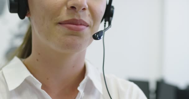 Close up de bela jovem operadora de pé e vestindo fone de ouvido no espaço de escritório brilhante — Vídeo de Stock