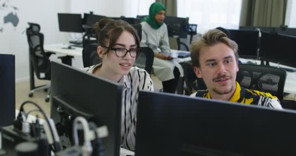 Dva příležitostně oblečení mladí obchodní kolegové, kteří používají počítač a mluví spolu během procesu v kanceláři — Stock video