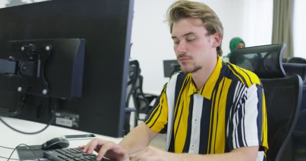 Красивий молодий бізнесмен, який працює за своїм настільним комп'ютером, сидить за своїм столом у стартап-офісі — стокове відео