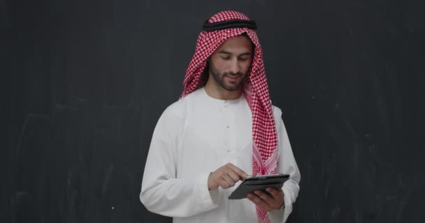 Portret van een jonge Arabische man in traditionele kleding voor een zwarte krijtbord rusing tablet — Stockvideo