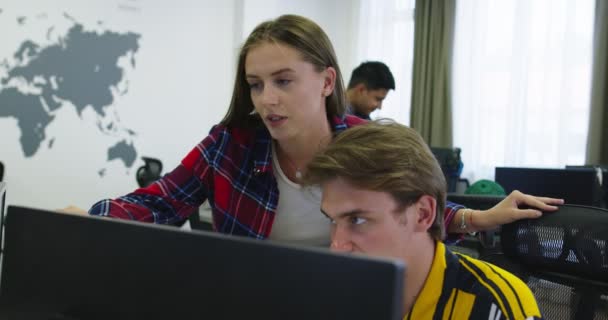 Twee casual geklede jonge collega 's van het bedrijfsleven met behulp van een computer en praten samen tijdens het proces bij het opstarten kantoor — Stockvideo