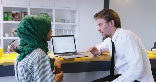 Två attraktiva människor blandad etnicitet diskuterar idéer med bärbar dator vid start kontor, kvinna med hijab möte man i start kontor — Stockvideo