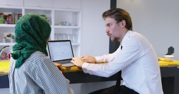Due persone attraenti etnicità mista discutendo idee utilizzando laptop presso l'ufficio startup, donna con hijab incontro uomo in ufficio startup — Video Stock