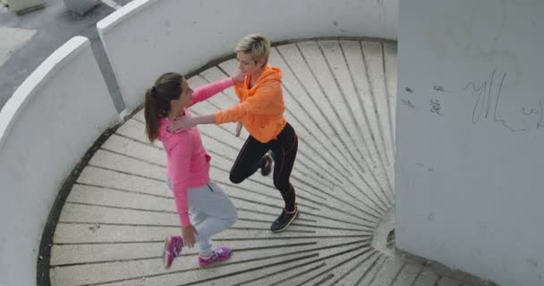 Две женщины расслабляются и растягиваются после тренировки, две молодые женщины растягиваются после бега в центре города, вид сверху — стоковое видео