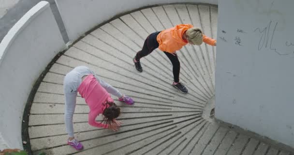 Dos mujeres relajándose y estirándose después del entrenamiento, dos mujeres jóvenes estirándose después de correr en el centro de la ciudad, vista superior — Vídeos de Stock