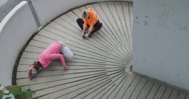 Twee vrouwen ontspannen en stretchen na de training, twee jonge vrouwen stretchen na het hardlopen in het centrum, bovenaanzicht — Stockvideo