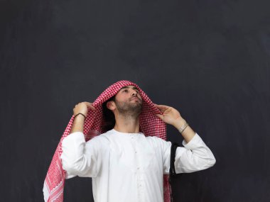 Geleneksel giysiler giyen genç Müslüman adamın portresi. Ramazan Kareem kavramını temsil eden siyah karatahtanın önünde duran mutlu Arap.