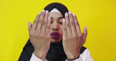 Genç ve güzel Afro-Amerikalı kız izole edilmiş sarı arka planda Müslüman başörtüsü takıyor ve el ele dua ediyor.