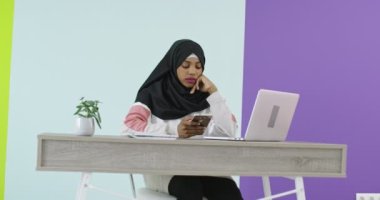 Başörtüsü takmış güzel ve mutlu bir kadın evde dizüstü bilgisayarla cep telefonu kullanıyor.. 