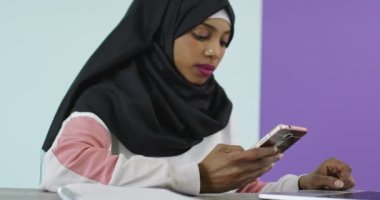 Başörtüsü takmış güzel ve mutlu bir kadın evde dizüstü bilgisayarla cep telefonu kullanıyor.. 