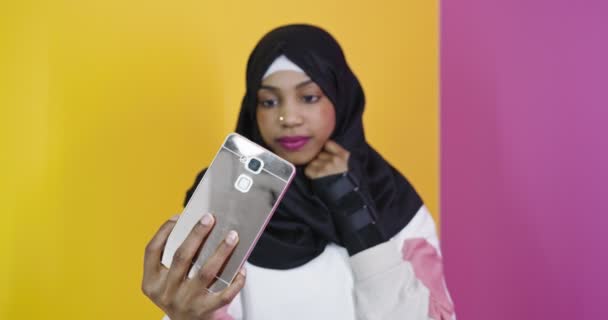 Cep telefonuyla tesettürlü mutlu Arap kadın renk arkaplanı üzerinde selfie çekiyor — Stok video