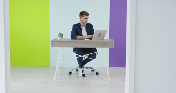 Красивый молодой человек, использующий ноутбук в современном офисе, фрилансер, работающий над новым домашним проектом — стоковое видео