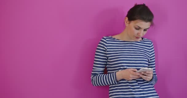 Досить молода дівчина-підліток друкує і читає текстове повідомлення на своєму новому мобільному телефоні на рожевому фоні — стокове відео