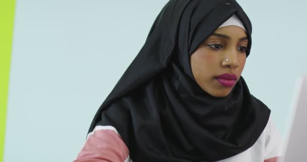 Mulher bonita e feliz no lenço da cabeça hijab usando telefone celular com computador portátil no escritório em casa. — Vídeo de Stock