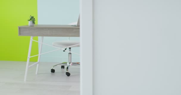 Стол с ноутбуком, стоящим в домашнем офисе перед пустой стеной — стоковое видео