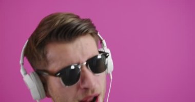 Kulaklık takan genç yakışıklı adam izole edilmiş arka planda müzik dinliyor dans ediyor ve kolları havada gülümsüyor.