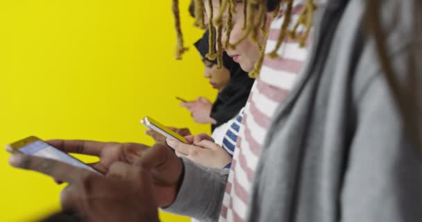Gruppo multiculturale di amici che utilizzano i telefoni cellulari Studenti in piedi in fila e digitando sugli smartphone sopra la parete a colori — Video Stock