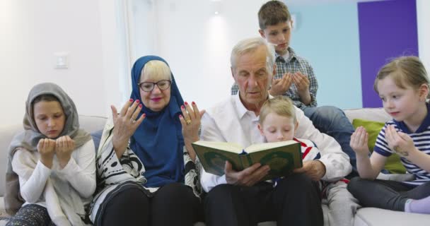 Traditionelle muslimische Großeltern mit Kindern, die den Koran lesen und gemeinsam auf dem Sofa beten — Stockvideo