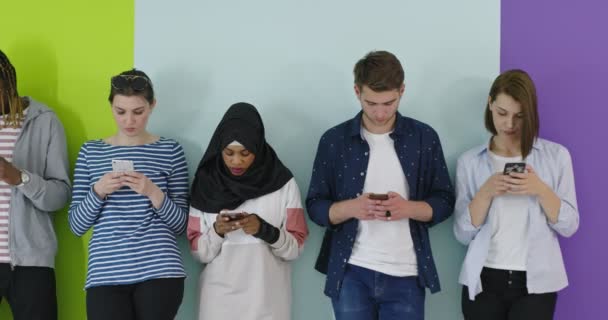Multikulturel gruppe af venner ved hjælp af mobiltelefoner Studerende stående i træk og skrive på smartphones over farve væg – Stock-video