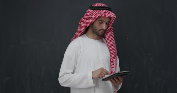 タブレットを使用して黒い黒板の前で伝統的な服の若いアラビア人の肖像画 — ストック動画