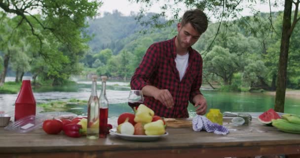 Man preparing meat and puting spices for barbeque and dinner beside river, preparing for dinner in nature in summer kitchen — Stock Video