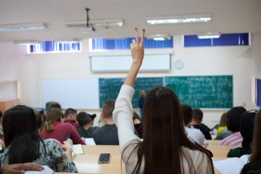 Bayan öğrenci sınıfta oturuyor ve elini kaldırıyor.
