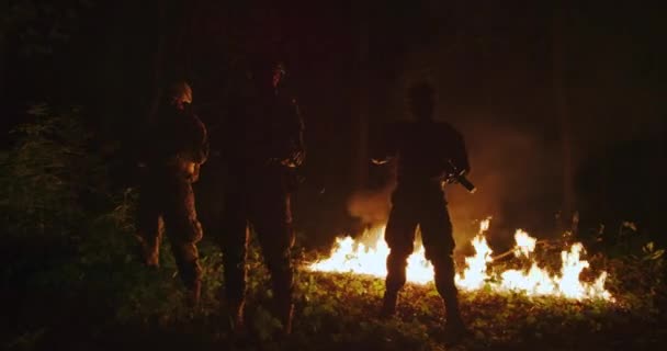 A katonák puskákat használnak az erdőben éjszaka, tűzzel a háttérben. — Stock videók