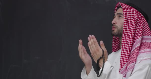 Μέση Ανατολή αραβική άνθρωπος με παραδοσιακά ρούχα μπροστά από το μαύρο μαυροπίνακα προσεύχεται — Αρχείο Βίντεο
