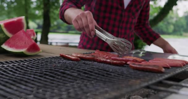 Primer plano de hombre cocinar carne en la barbacoa al aire libre en la naturaleza junto al río y prealabanza para la cena en la naturaleza — Vídeo de stock