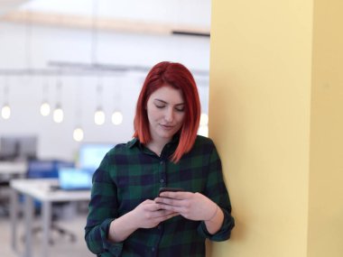 Ofisteki kızıl saçlı iş kadını akıllı telefon kullanıyor.
