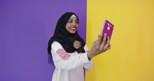 Porträtt av leende afrikansk svart muslim flicka, poserar på färg studio bakgrund tar selfie foto — Stockvideo