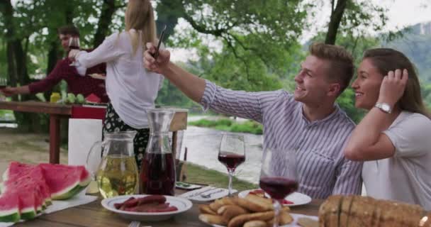 Молодая счастливая пара делает селфи во время пикника французский ужин на открытом воздухе во время летнего отдыха на берегу реки на красивой природе — стоковое видео