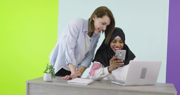Mångfald Etniska kvinnor möts i ämbetet. Leende flicka i Hijab arbetar på laptop, blond tittar på skärmen. — Stockvideo
