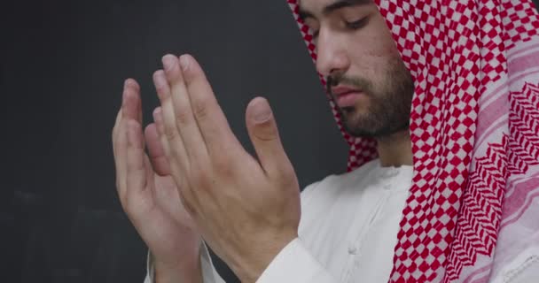 Homem em roupas tradicionais na frente do quadro negro rezando com as mãos bem abertas — Vídeo de Stock