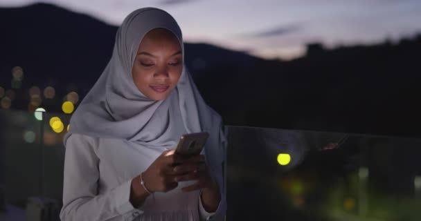 Moslim vrouw sms 'en op smartphone met bokeh stad licht op de achtergrond — Stockvideo