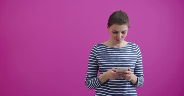 Chica escribiendo y leyendo mensajes de texto en su nuevo teléfono celular moderno móvil sobre un fondo rosa — Vídeos de Stock
