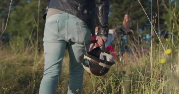 Zbliżenie hipstera trzymając cykuty i idąc w kierunku grupy przyjaciół, którzy bawią się w porannym słońcu obok off road car — Wideo stockowe