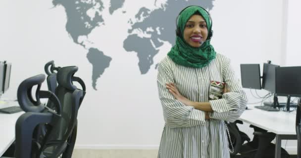 Feliz mujer de negocios islámica con hijab usando un auricular mientras está de pie en la oficina moderna — Vídeos de Stock
