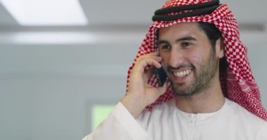 Arap işadamı evde akıllı telefon kullanırken geleneksel kıyafetler giyiyor.