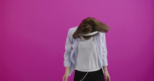 Grappige vrouw met koptelefoon luisteren naar muziek en dansen over kleur backgorund — Stockvideo