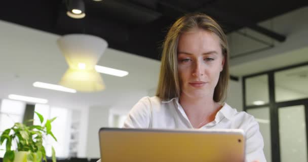 Hermosa chica joven con el pelo largo celebración tableta digital de lectura de correo electrónico en el sofá en la oficina de inicio — Vídeos de Stock