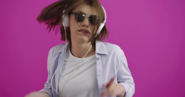 Zabawna kobieta nosząca słuchawki słuchające muzyki i tańczące nad kolorem backgorund — Wideo stockowe