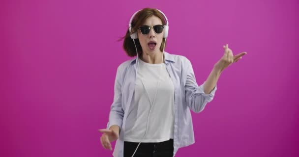 Grappige vrouw met koptelefoon luisteren naar muziek en dansen over kleur backgorund — Stockvideo