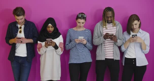 Глобальное общение. Студенты пишут смс на смартфонах, опираясь на цветную стену — стоковое видео