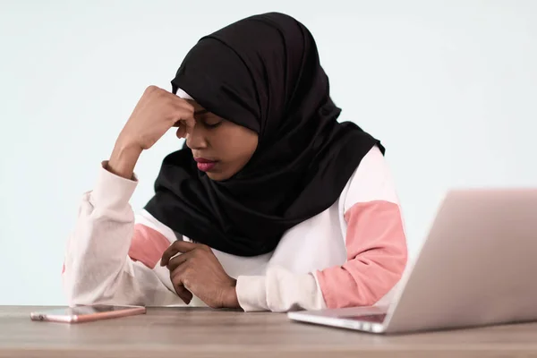 Дівчина в хіджабі розчарована і сумно сидить у своєму домашньому офісі і використовує ноутбук — стокове фото