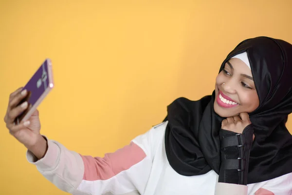 Mulher muçulmana africana com um belo sorriso leva uma selfie com um telefone celular — Fotografia de Stock