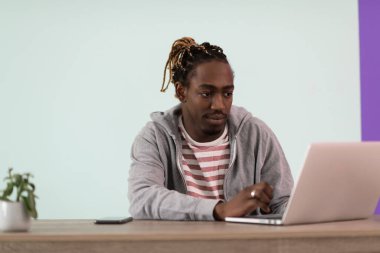 Bir afro genç adam salgın sırasında evinde oturuyor ve online toplantı için laptop kullanıyor. .