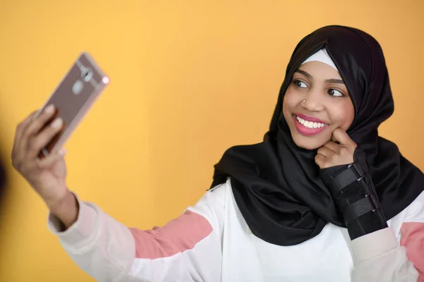 Mulher muçulmana africana com um belo sorriso leva uma selfie com um telefone celular — Fotografia de Stock